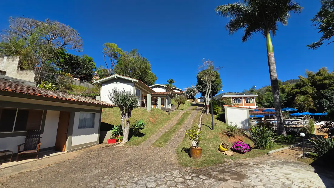 Caminho gramado entre os chalés, com jardim e as montanhas ao fundo