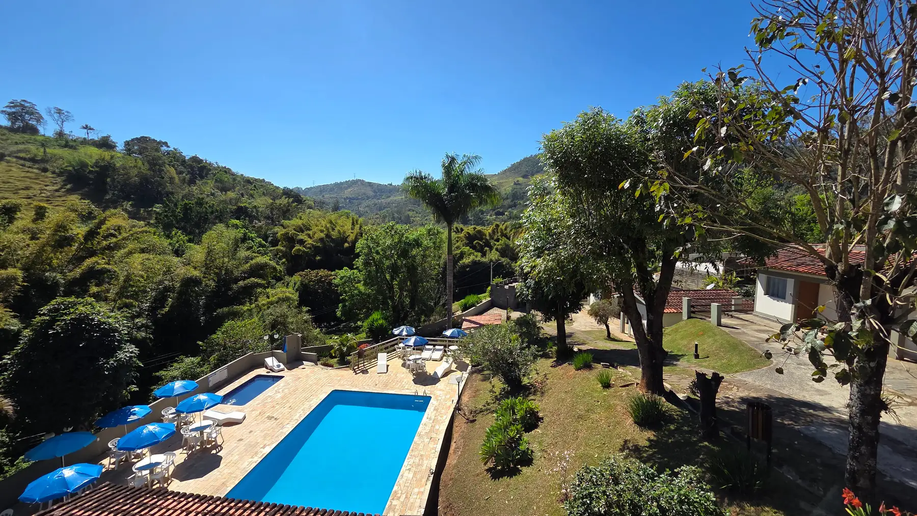 Vista do alto da pousada, com a piscina, o jardim e as montanhas ao fundo