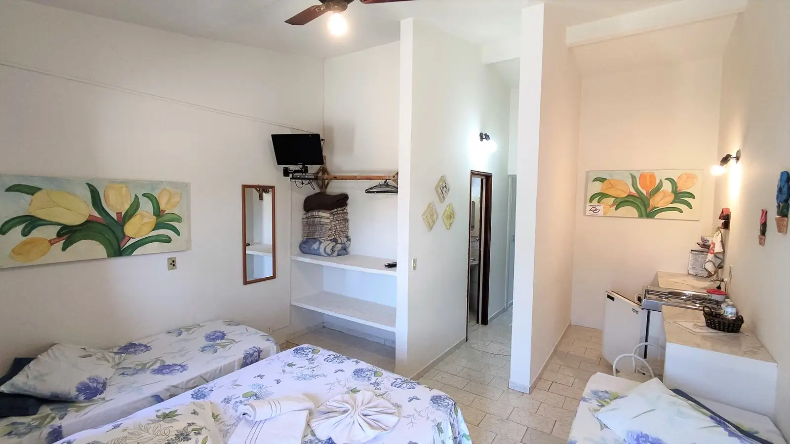 Quarto do Chalé Familiar, com duas camas, espelho, TV e a passagem para a cozinha