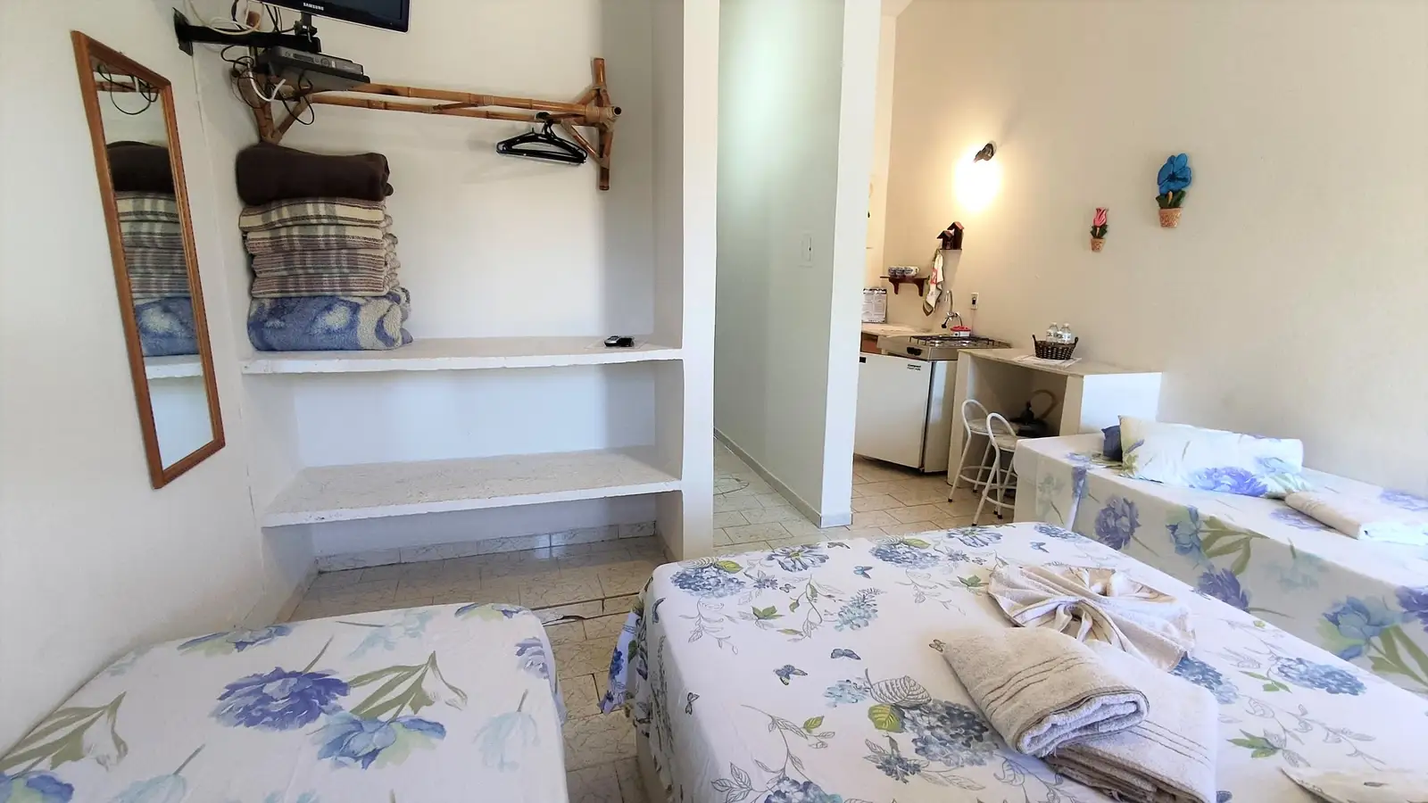 Quarto do Chalé Familiar, com prateleira de toalhas e a cozinha ao fundo