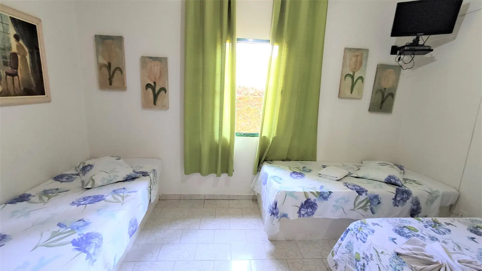 Segundo quarto do Chalé Familiar, com duas camas e janela de cortina verde