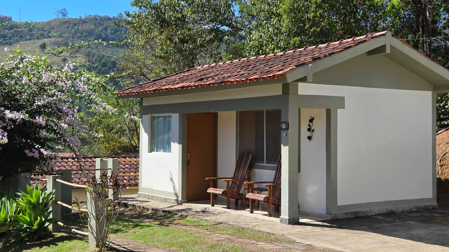 Fachada do Chalé Master, com varanda, cadeiras de madeira e uma árvore florida ao lado