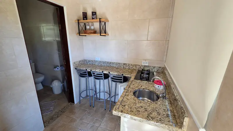 Cozinha de um dos chalés, com cooktop, pia e bancada de granito com banquetas