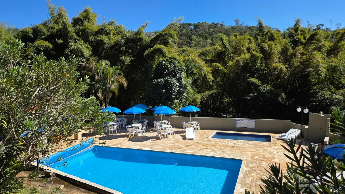 Piscina da pousada com guarda-sóis azuis e a mata em volta