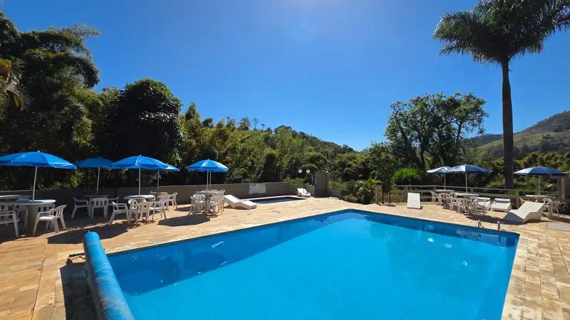 Piscina aquecida com guarda-sóis azuis e a mata ao redor, em dia de sol