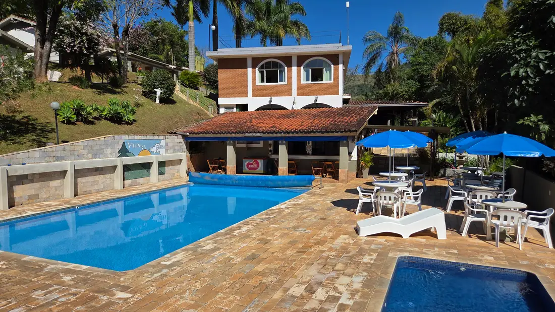 Lanchonete da pousada ao lado da piscina, com as mesas e guarda-sóis azuis na frente