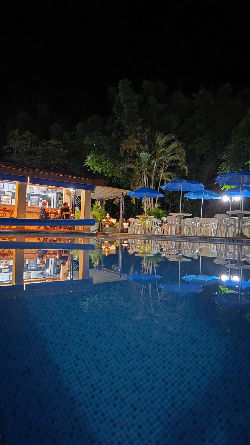 Piscina iluminada à noite, com o restaurante refletido na água