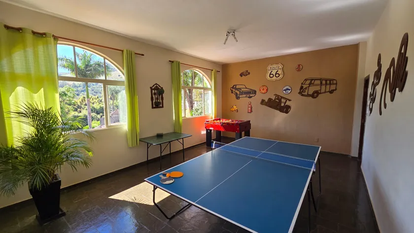 Sala de jogos com mesa de ping-pong e pebolim, de frente para as janelas