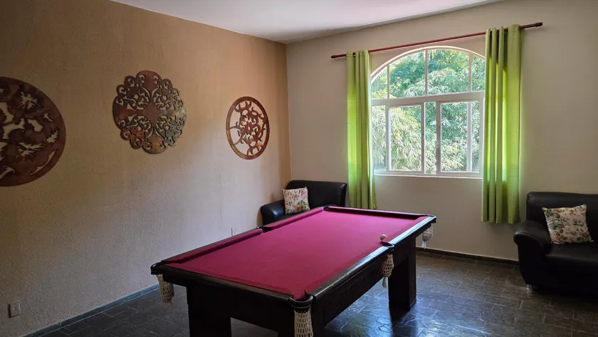 Sala com mesa de sinuca, poltrona e janelas para a mata