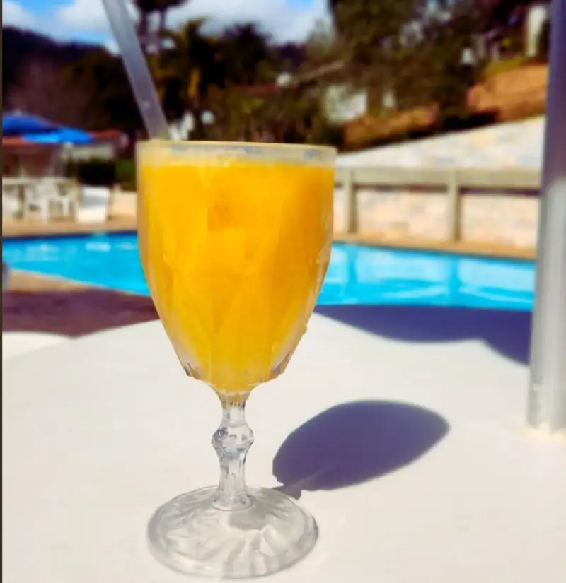 Taça de suco de laranja com canudo, na mesa à beira da piscina